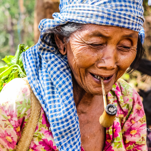 Close-up van een oudere Cambodiaanse vrouw met een pijp in haar mond en een mand met geplukte bosproducten op haar rug.